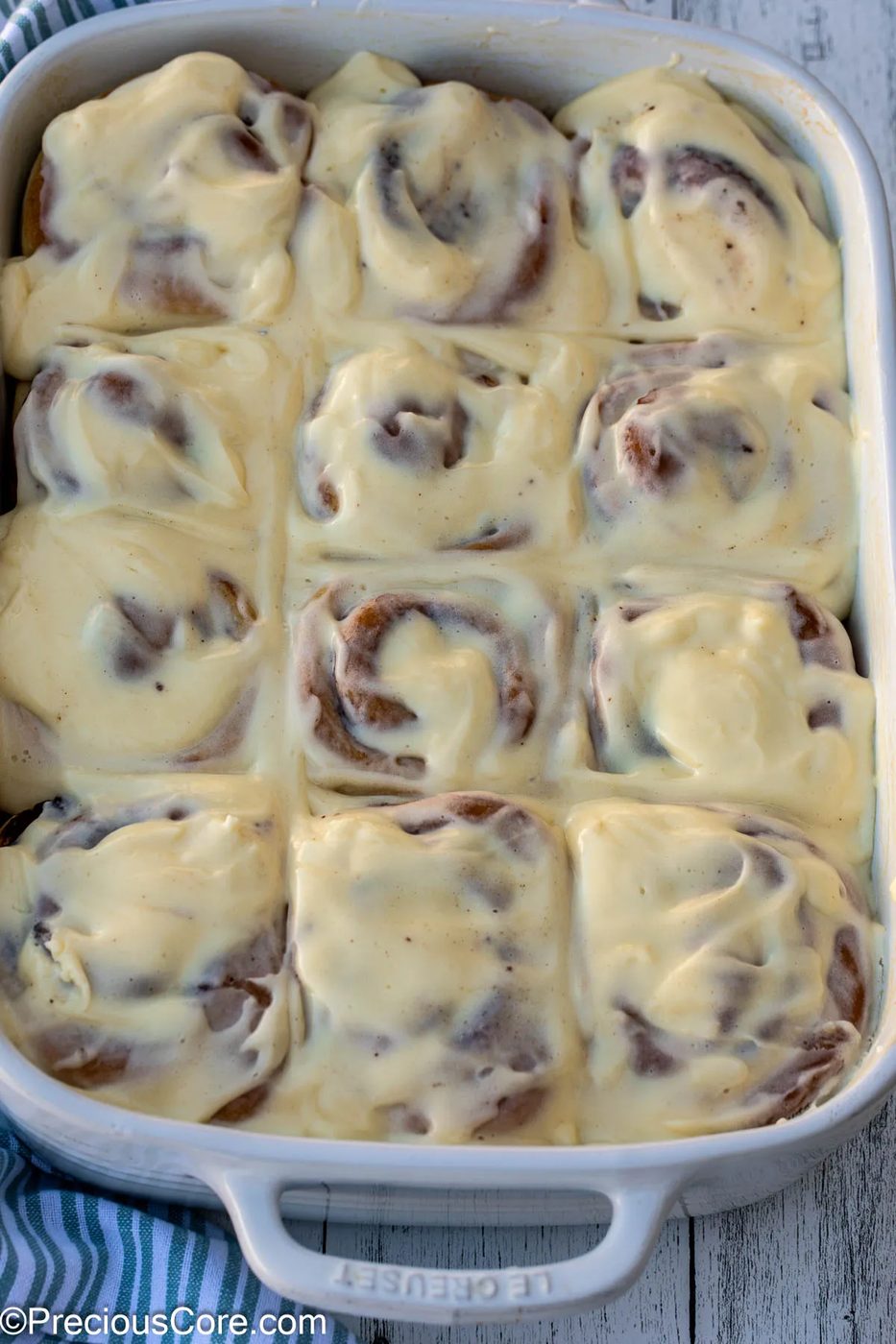 Cinnamon Rolls completely covered with cream cheese frosting in a white baking dish.