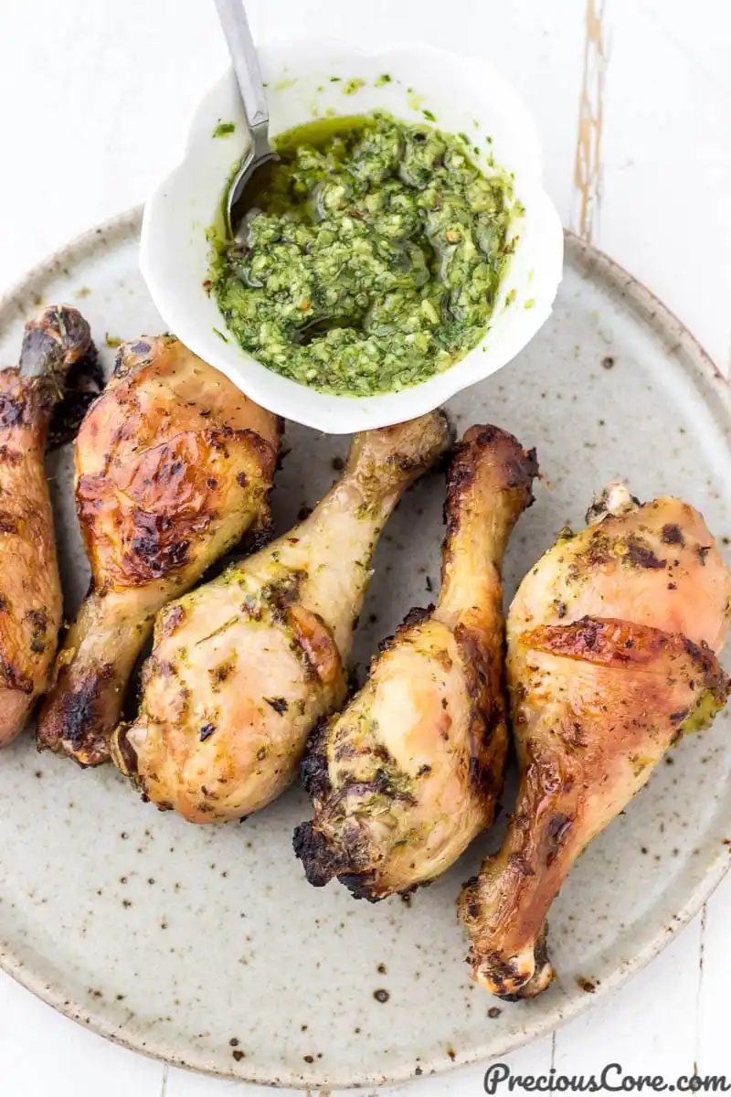 Grilled chicken on a plate with a bowl of green sauce nearby