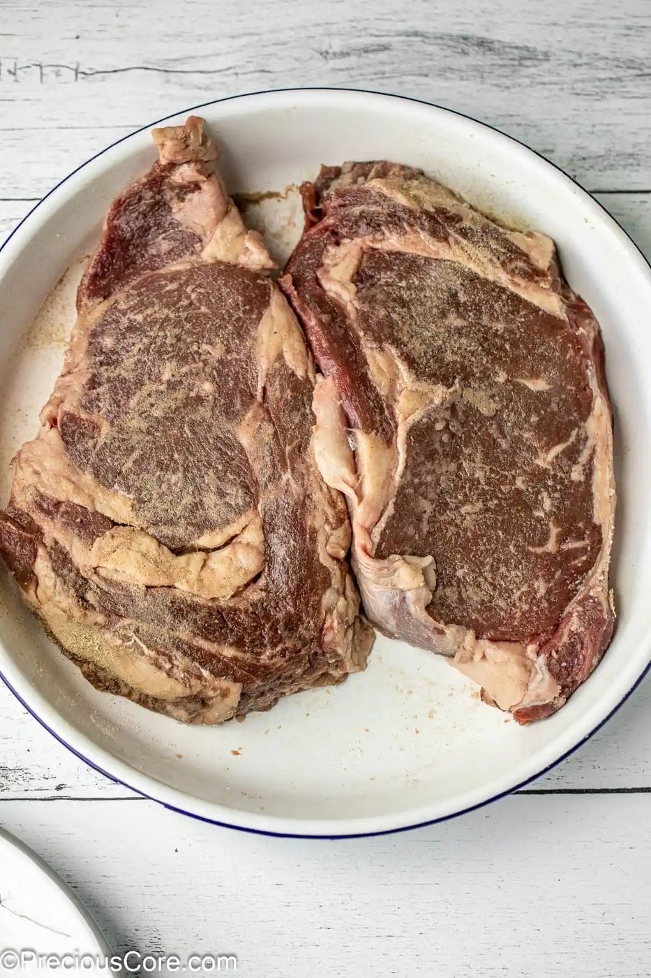 2 seasoned steaks in a white bowl.