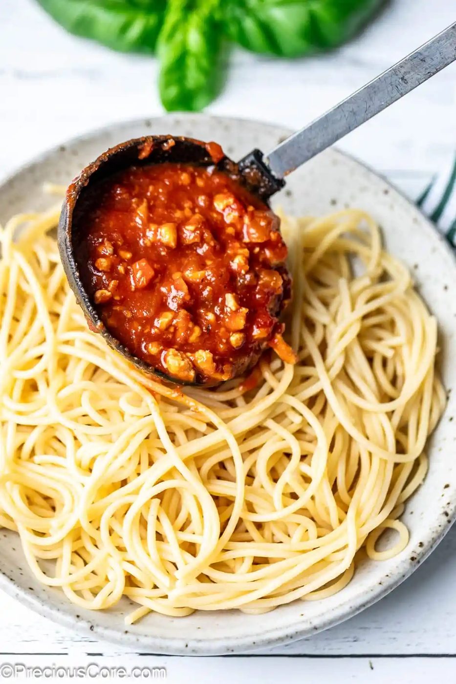 Pouring red meaty sauce over cooked spaghetti.