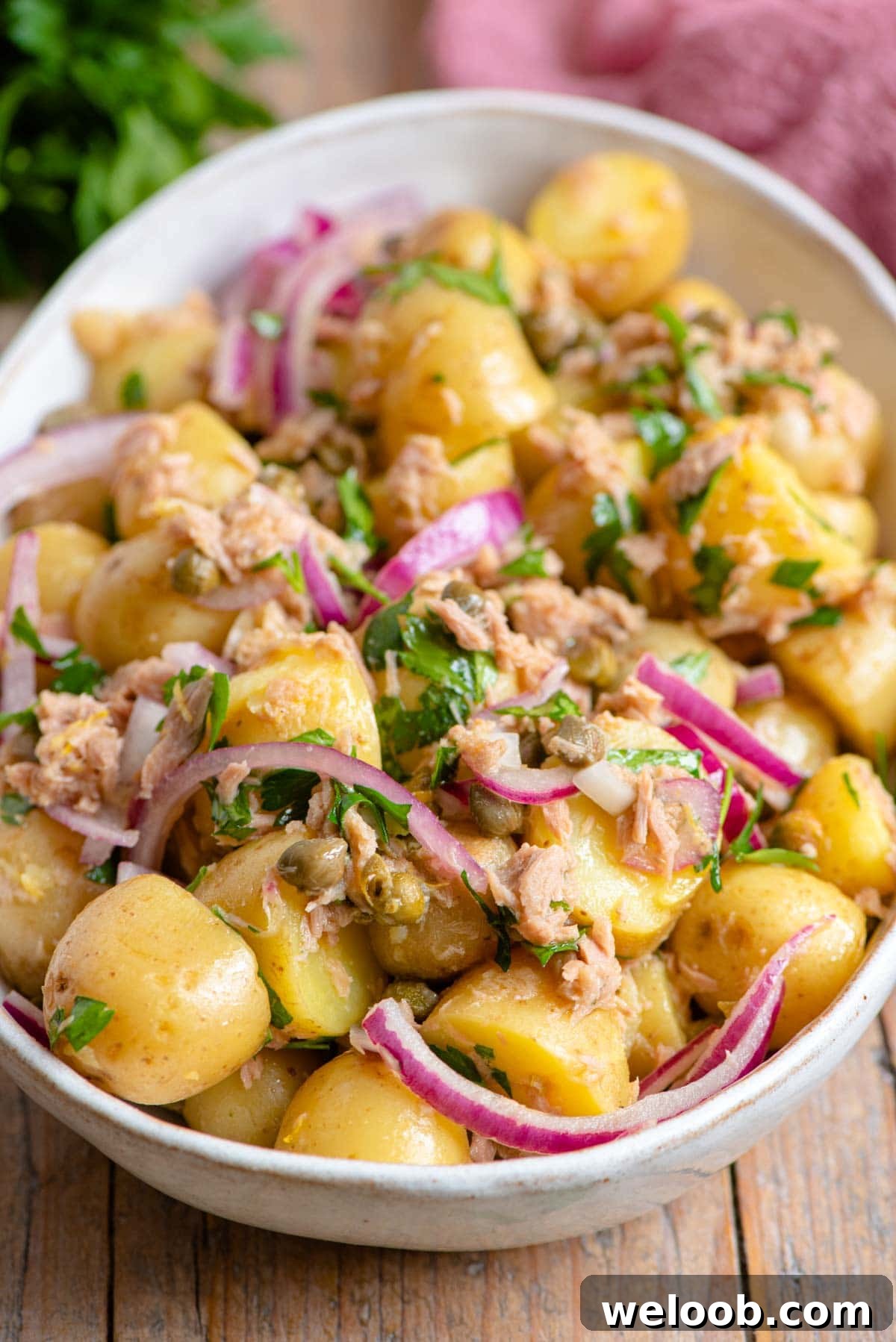 A close up of a tuna potato salad with red onion and capers in a bowl