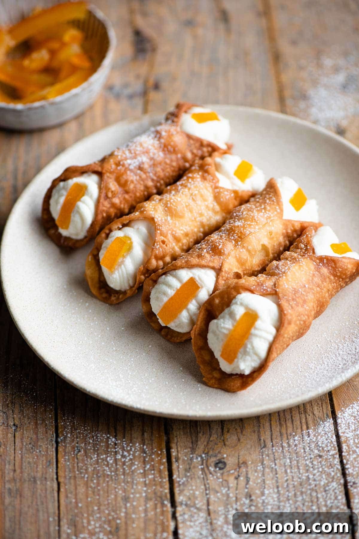 Four cannoli on a plate filled with ricotta and a slice of candied orange