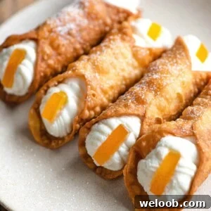A close up of four homemade cannoli filled with ricotta and topped with candied orange on a plate