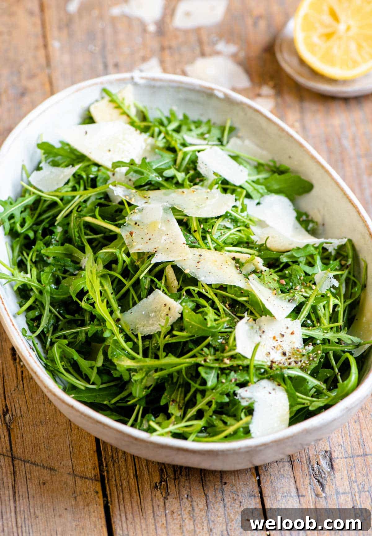 An arugula salad in a large serving bowl with shavings of parmesan