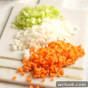 A close up of finely chopped carrot, celery and onion on a cutting board