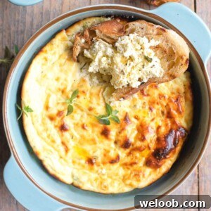 A close up cropped square image of baked ricotta in a blue ceramic round dish topped with a slice of crusty bread dipped in