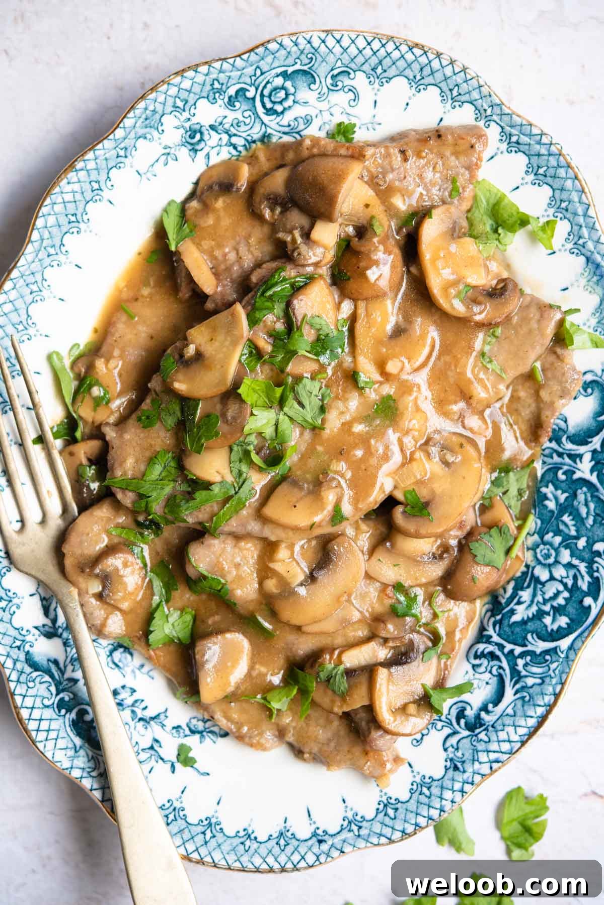 An overhead shot of veal marsala on a blue platter with mushrooms and parsley