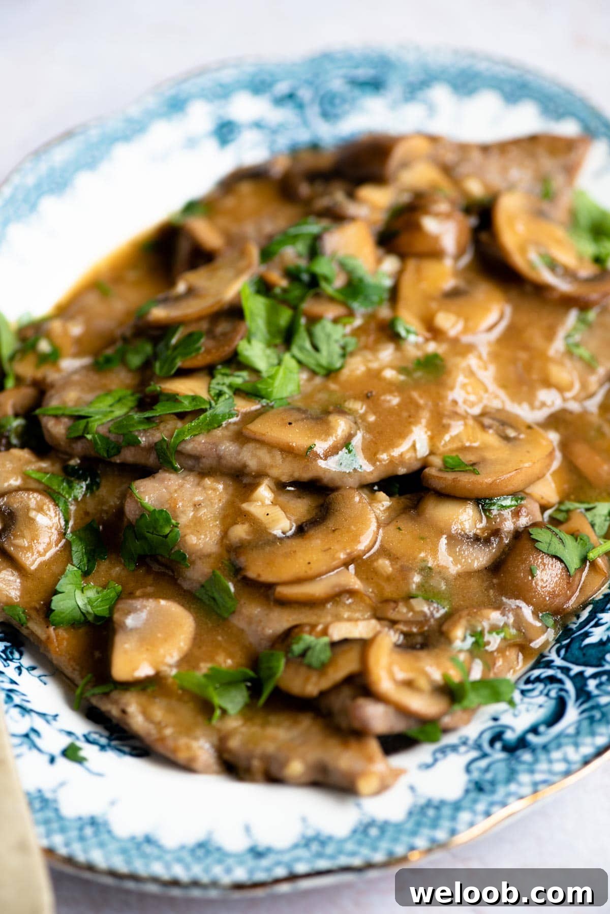 A close up of veal marsala with lots of sauce, mushrooms and parsley