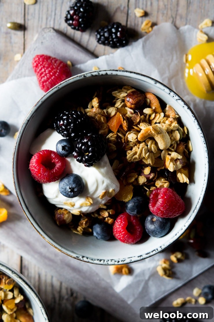 An overhead shot of healthy granola in a small bowl topped with berries and yogurt with scattered berries in the background