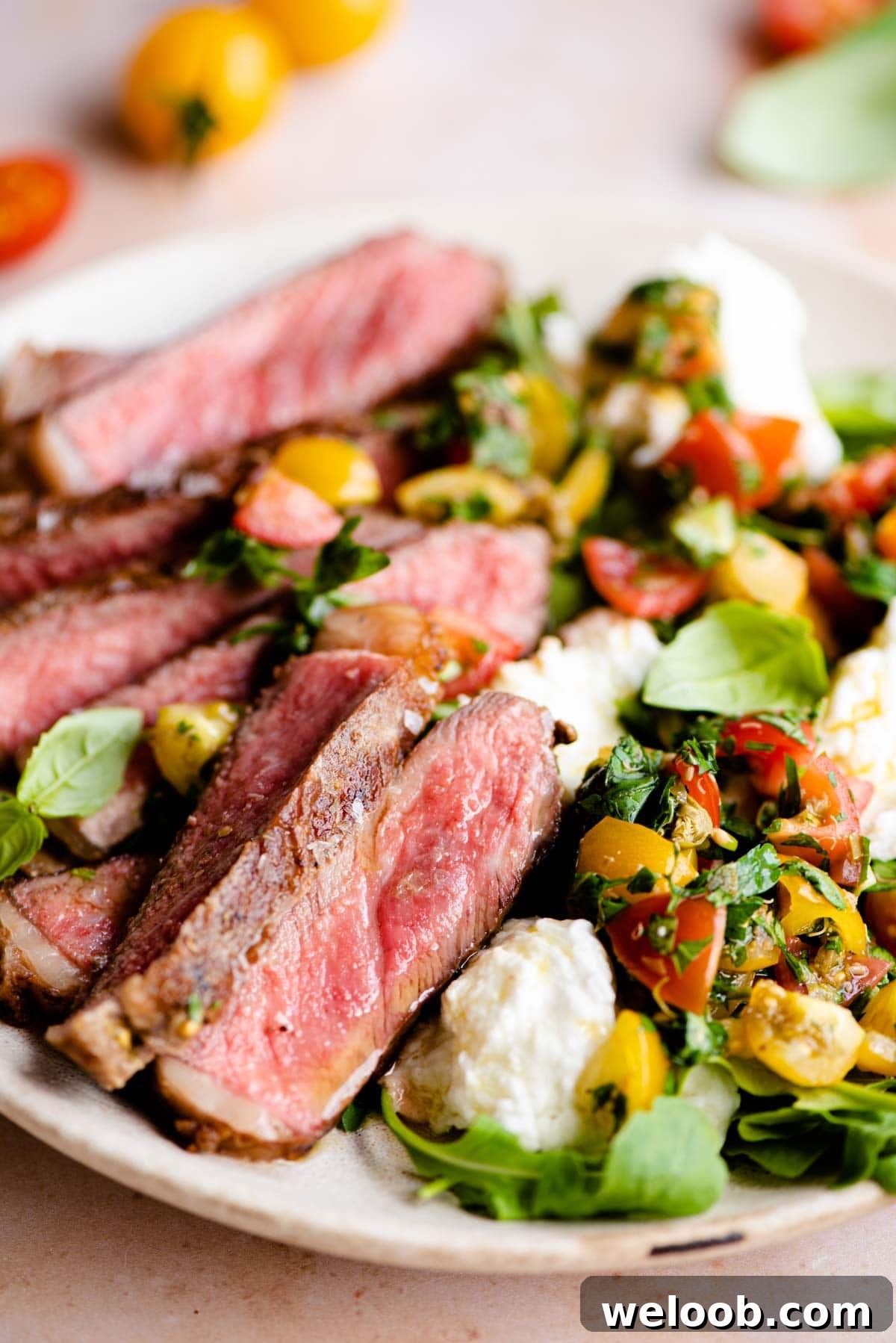 A close up of steak tagliata on a plate with tomato and mozzarella