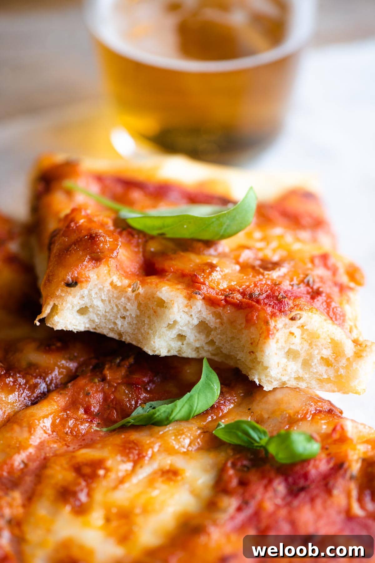 A close up of a slice of focaccia pizza with a bite out so you can see the fluffy texture