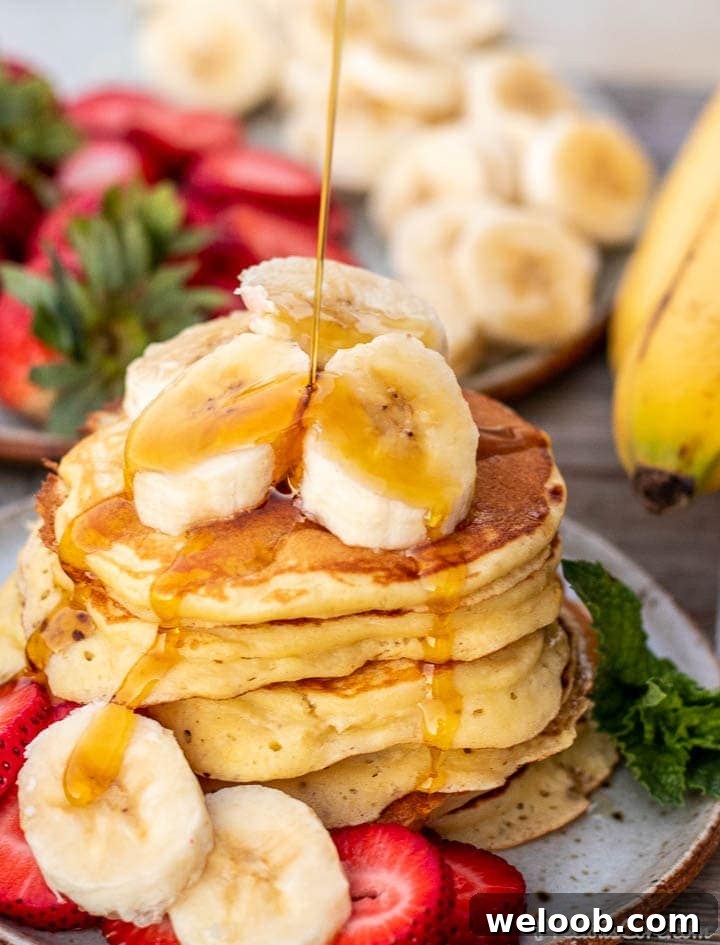 Stack of banana slices on a plate, banana slices on the stack and maple syrup pouring on top
