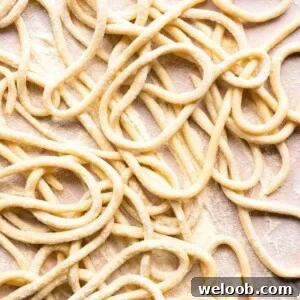 A close up of pici pasta on a neutral background
