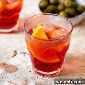 A close up of an Americano cocktail in a glass with orange and ice