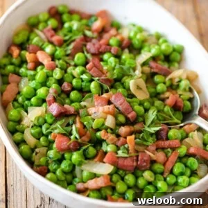 A close up of peas and pancetta in an oval serving dish on a wooden surface