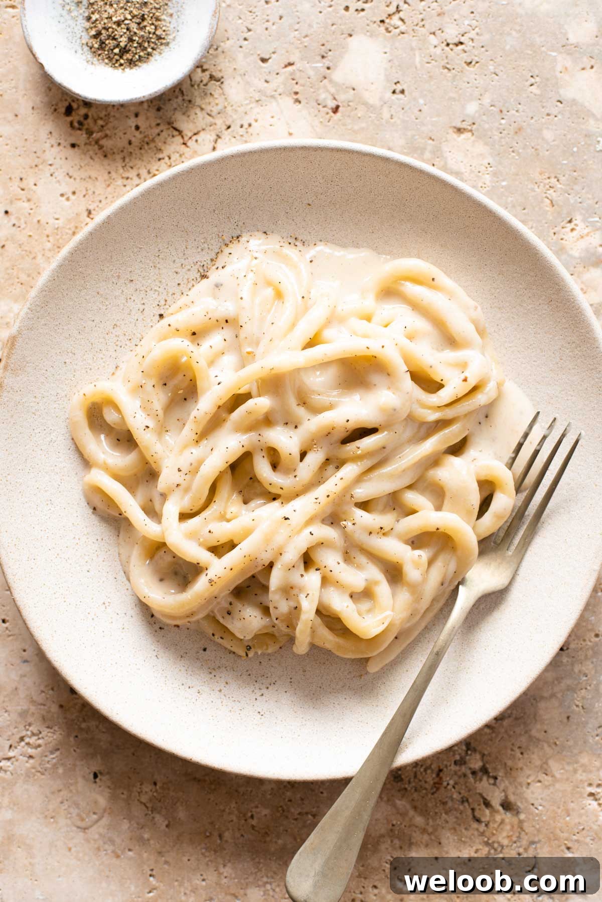 An overhead shot of pici pasta with cacio e pepe sauce on a plate