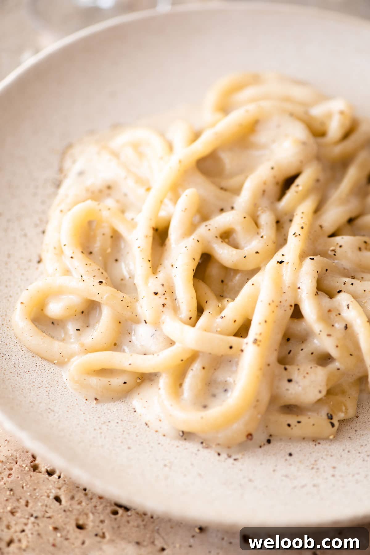 A close up of pici pasta with cacio e pepe sauce on a plate