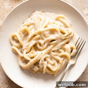 A close up of cacio e pepe with pici pasta on a plate with a fork