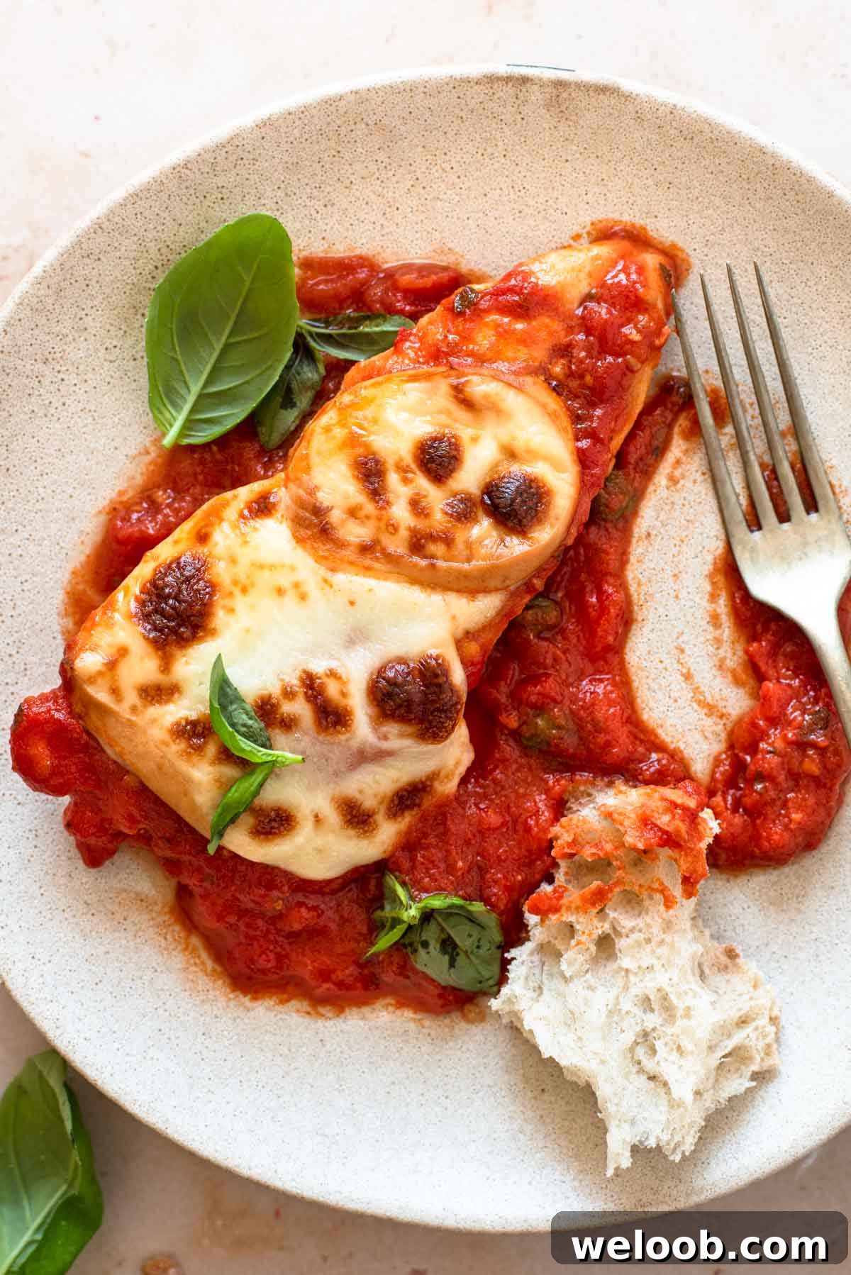 Smoked Scamorza Chicken Pizzaiola with Tomato and Herbs 2 A close up of a piece of chicken pizzaola on a plate with crusty bread and basil leaves