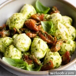 A close up of mozzarella bocconcini in a bowl with pesto and tomatoes