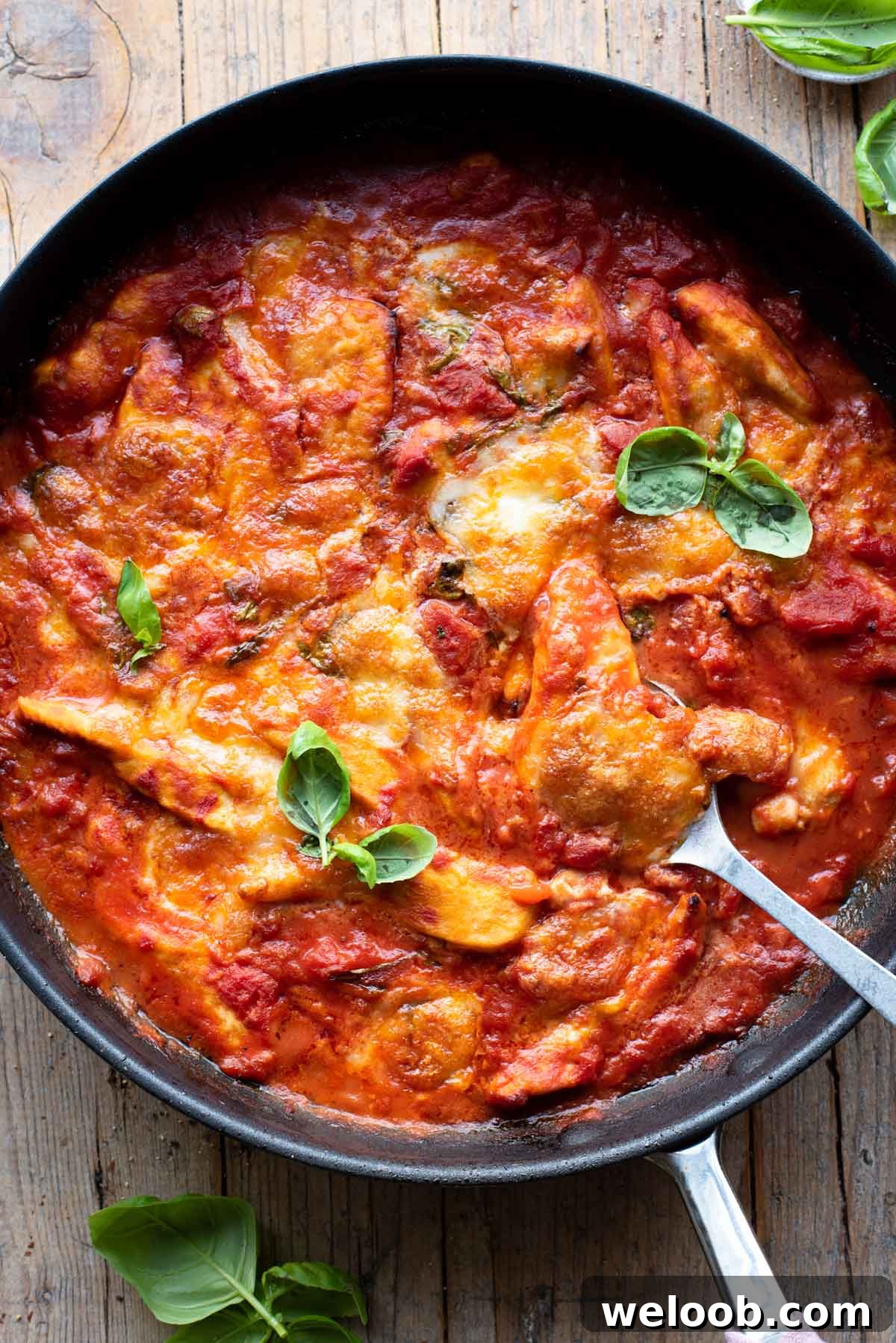 An overhead shot of a skillet with chicken baked in tomato sauce and topped with mozzarella