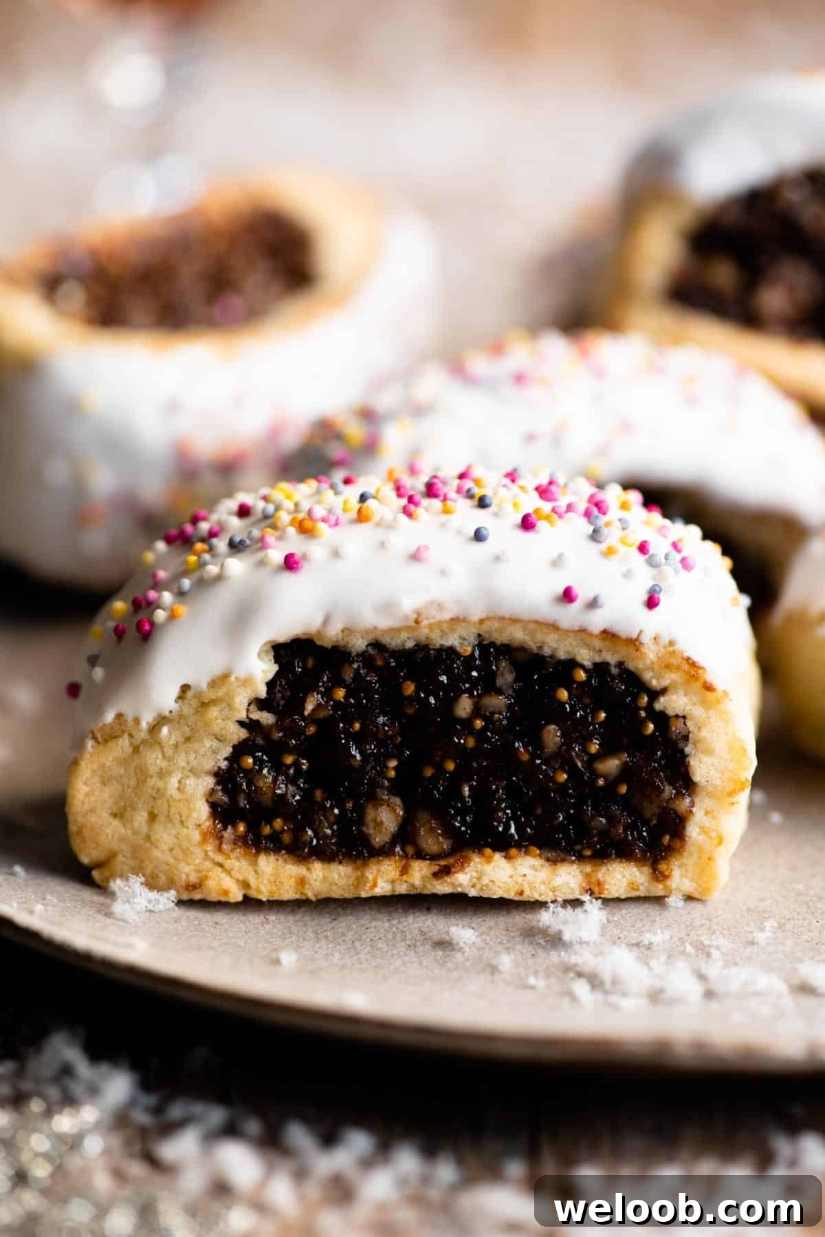 A close up of a cuccidati cookie topped with white icing and coloured sprinkles.