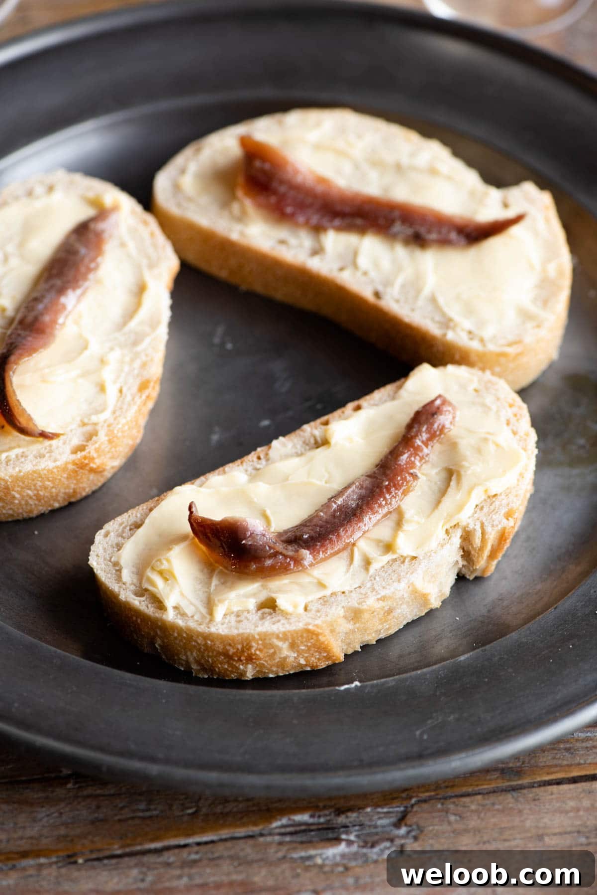 A close up of a slice of bread spread with butter and topped with an anchovy