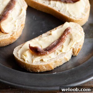 A close up of a slice of bread and butter topped with an anchovy