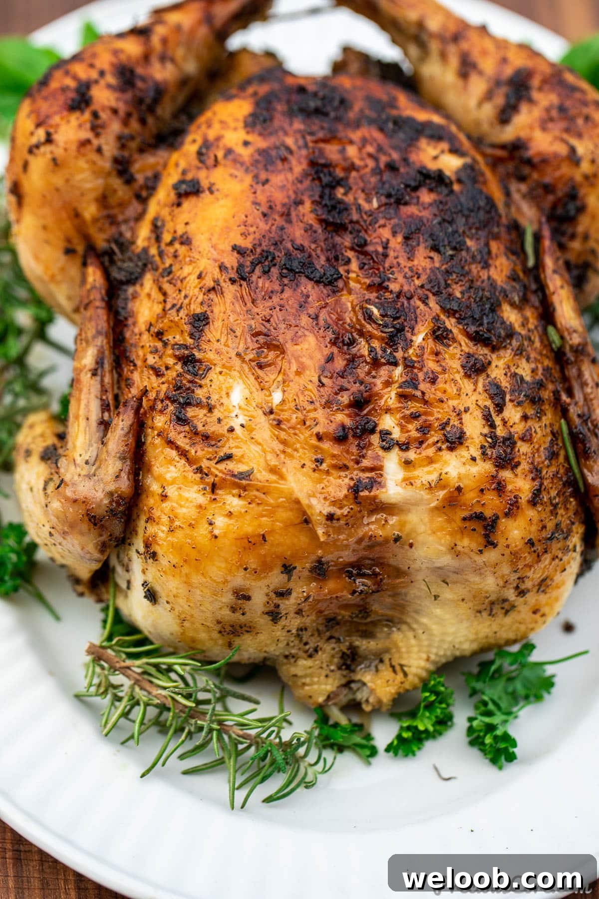 Whole herb roasted chicken on a platter, garnished with fresh herbs.
