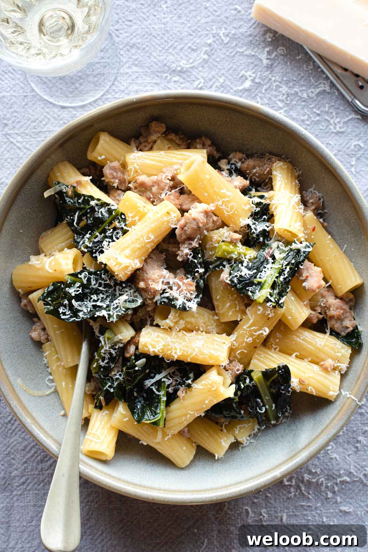 An overhead shot of a bowl of pasta with kale and sausage with a glass of wine at the side