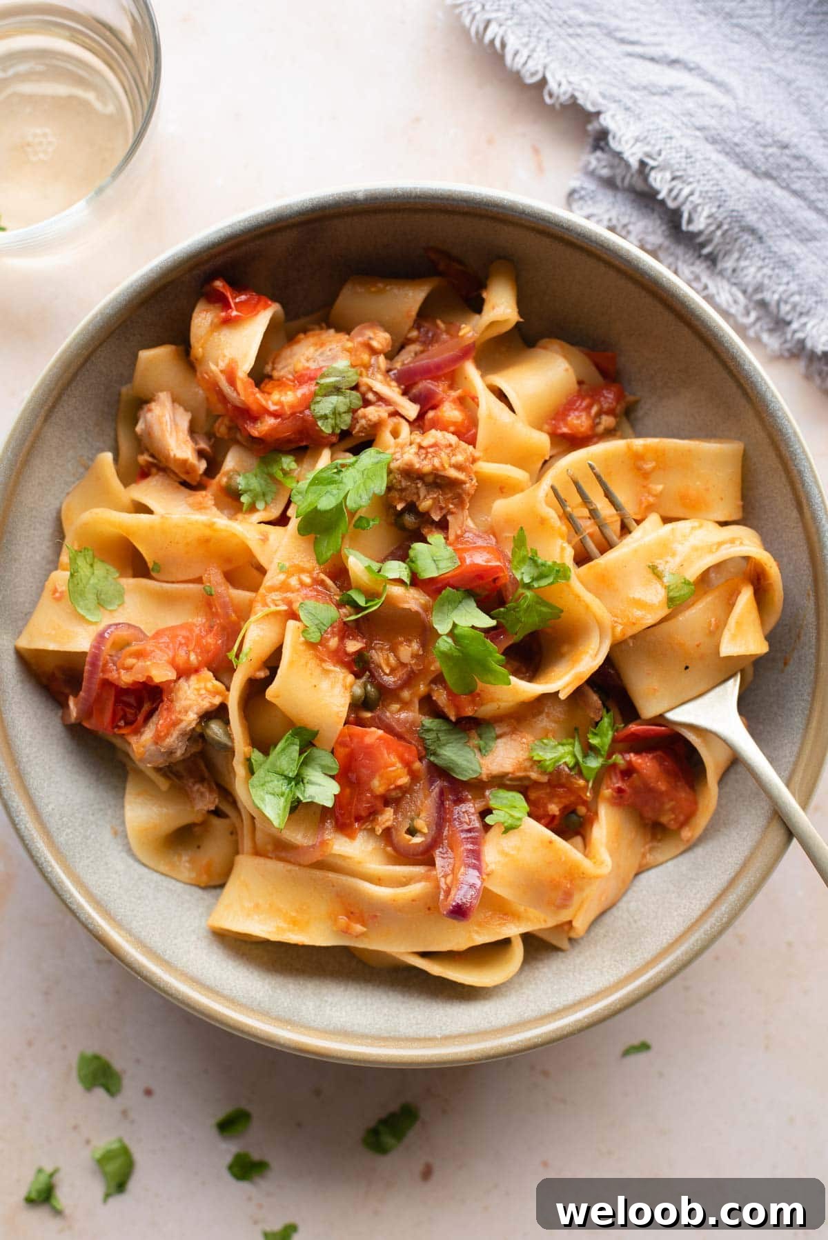 An overhead shot of tuna pasta in a bowl with tomatoes, capers and parsley