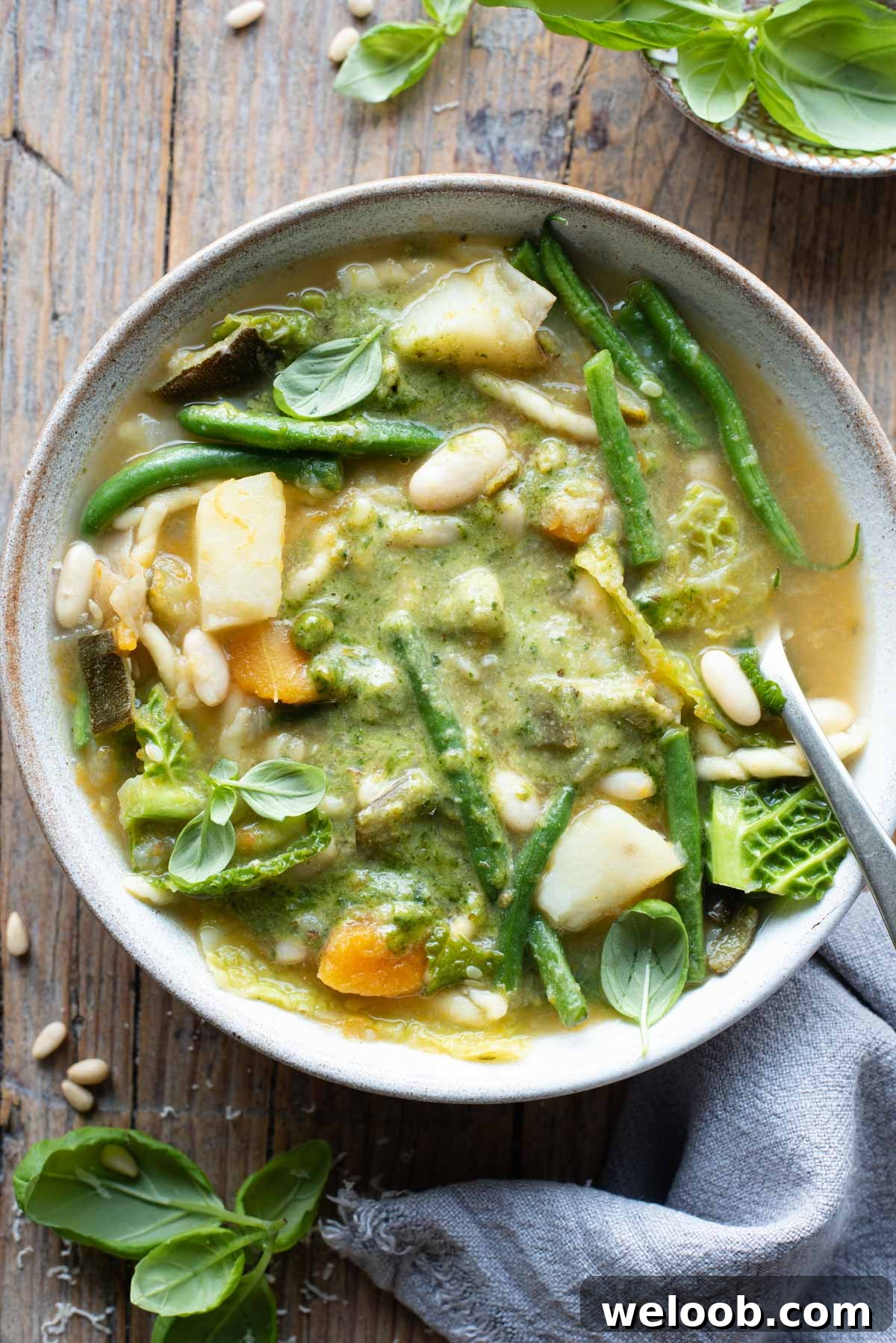 An overhead shot of a bowl of Ligurian minestrone with lots of vegetables and basil pesto sitting on a wooden background