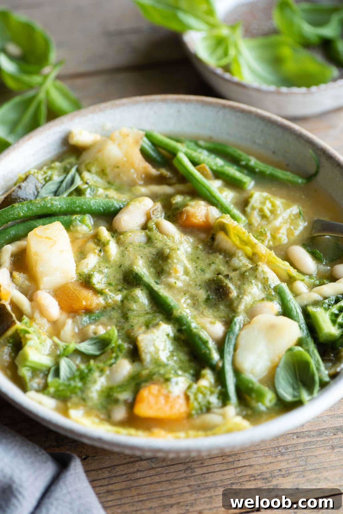 A close up of a bowl of minestrone soup with lots of mixed vegetables and basil pesto