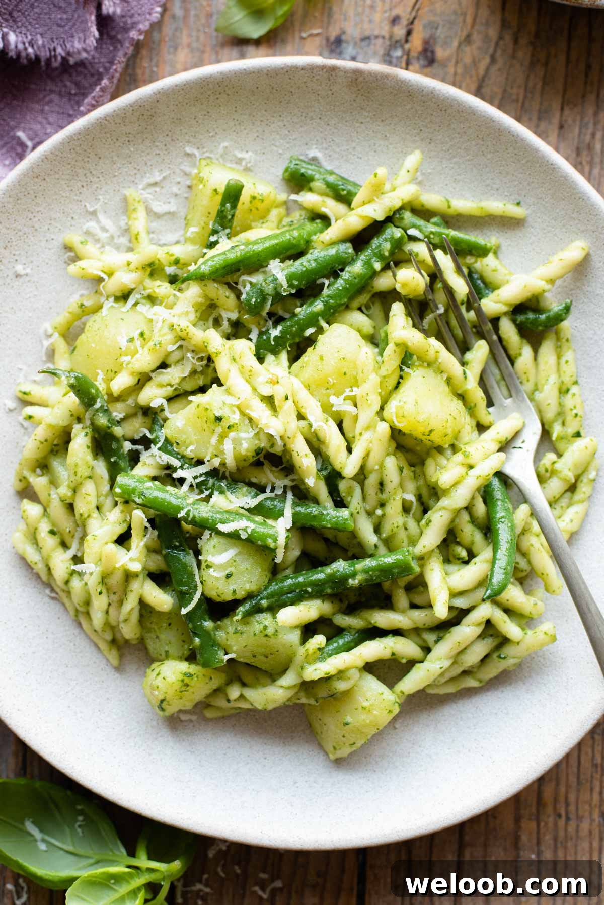 A close up of trofie pasta with pesto, potatoes and green beans on a plate with a fork at the side
