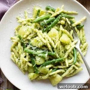 A close up of pesto pasta on a plate with potatoes and green beans