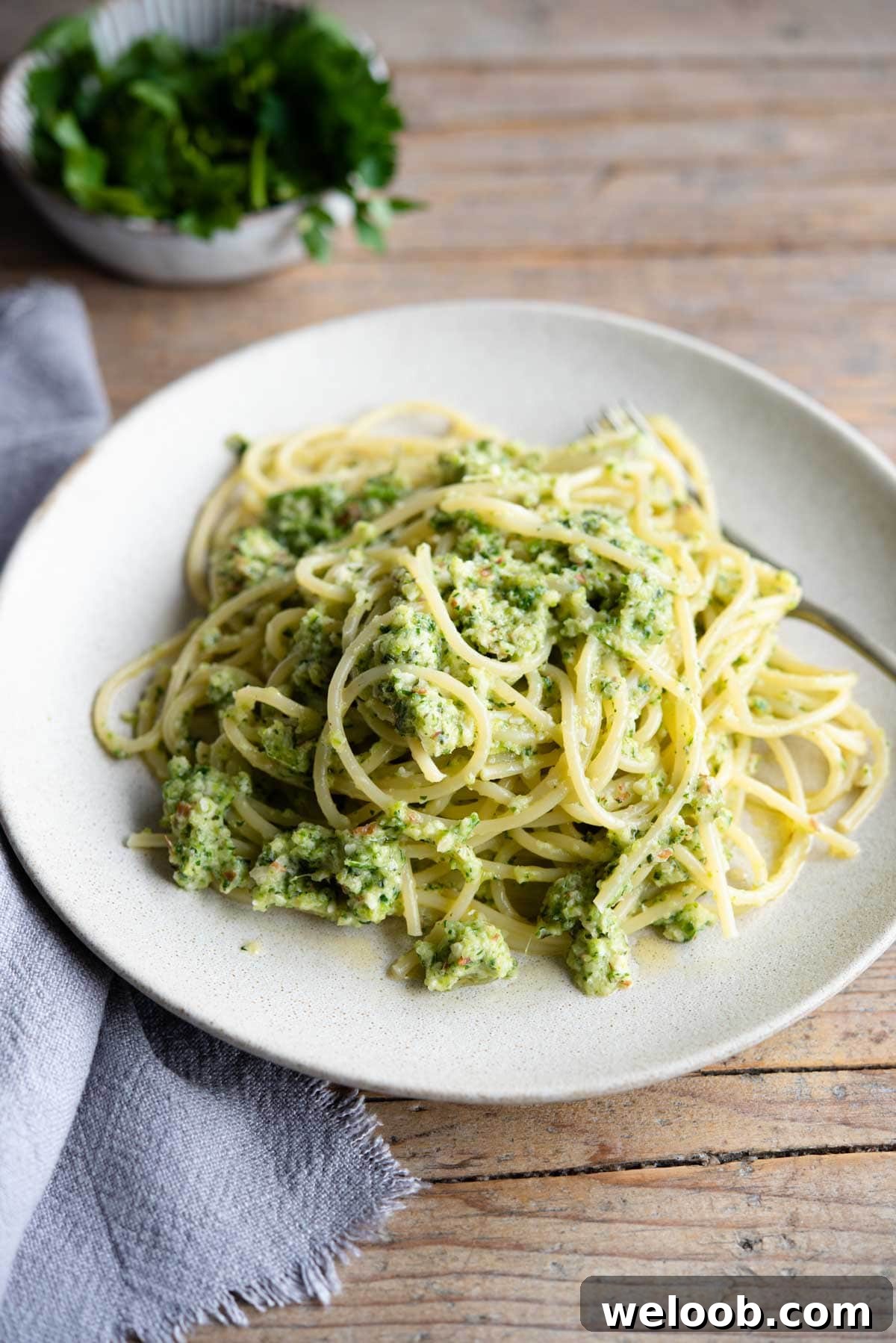 A plate for zucchini pesto pasta on a wooden surface with a blue towel at the side