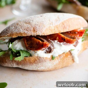 A close up of a ciabatta sandwich filled with arugula, burrata, anchovies and tomatoes
