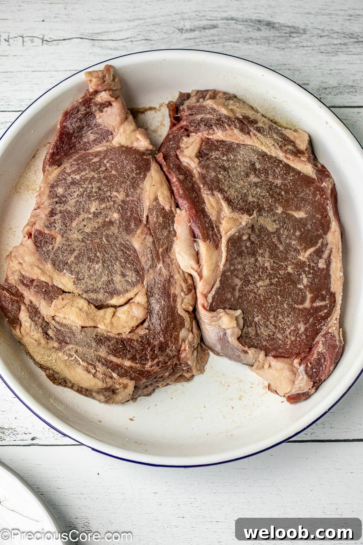 Perfect Pan-Seared Ribeye Steak with Crispy Crust and Juices 5 2 seasoned steaks in a white bowl.