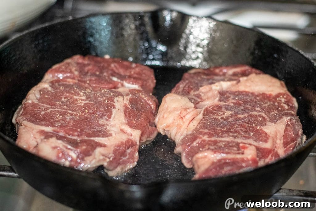 Perfect Pan-Seared Ribeye Steak with Crispy Crust and Juices 6 Raw ribeye steak in a cast iron skillet.
