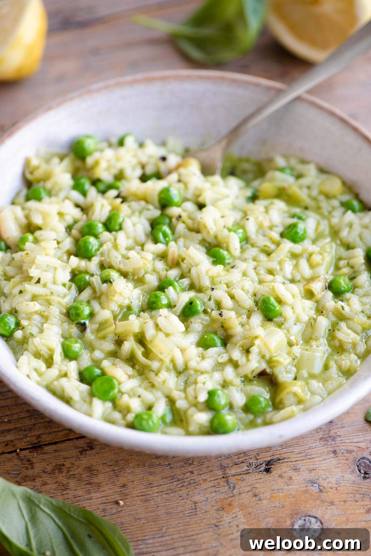 A side shot of a pea and pesto risotto in a bowl in a wooden surface with a fork at the side