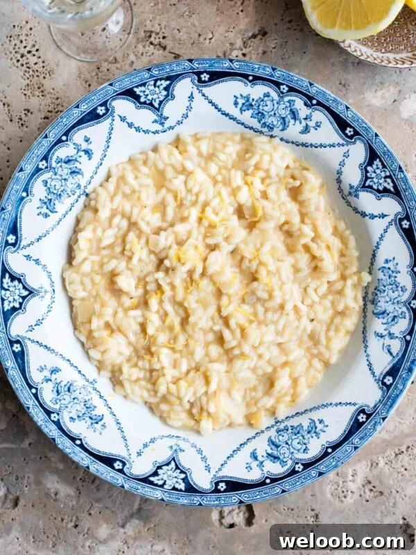 An overhead shot of a bowl of lemon risotto on a travertine surface with lemons at the side.