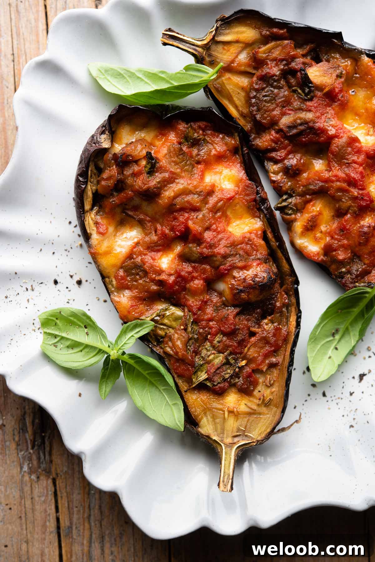 Two stuffed eggplants on a scalloped edged plate with basil scattered around.