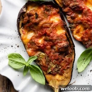 A close up of half a stuffed eggplant on a plate topped with fresh basil.