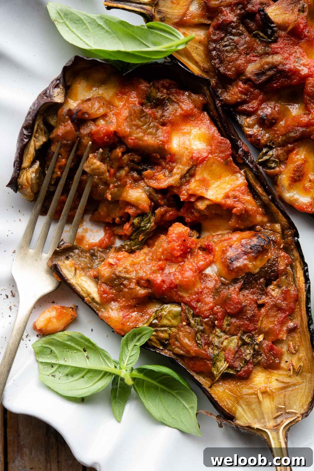 A close up of half an eggplant stuffed with tomato and mozzarella cut open on a plate.