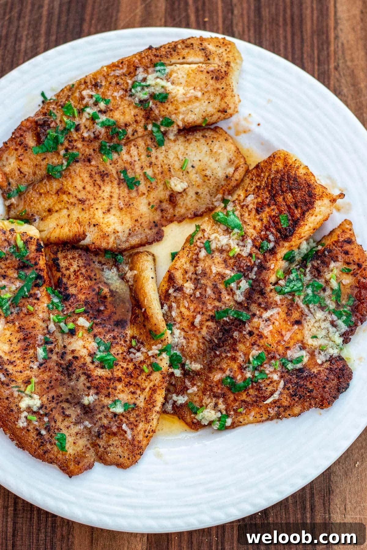 Lemon butter tilapia fillets on a white plate.