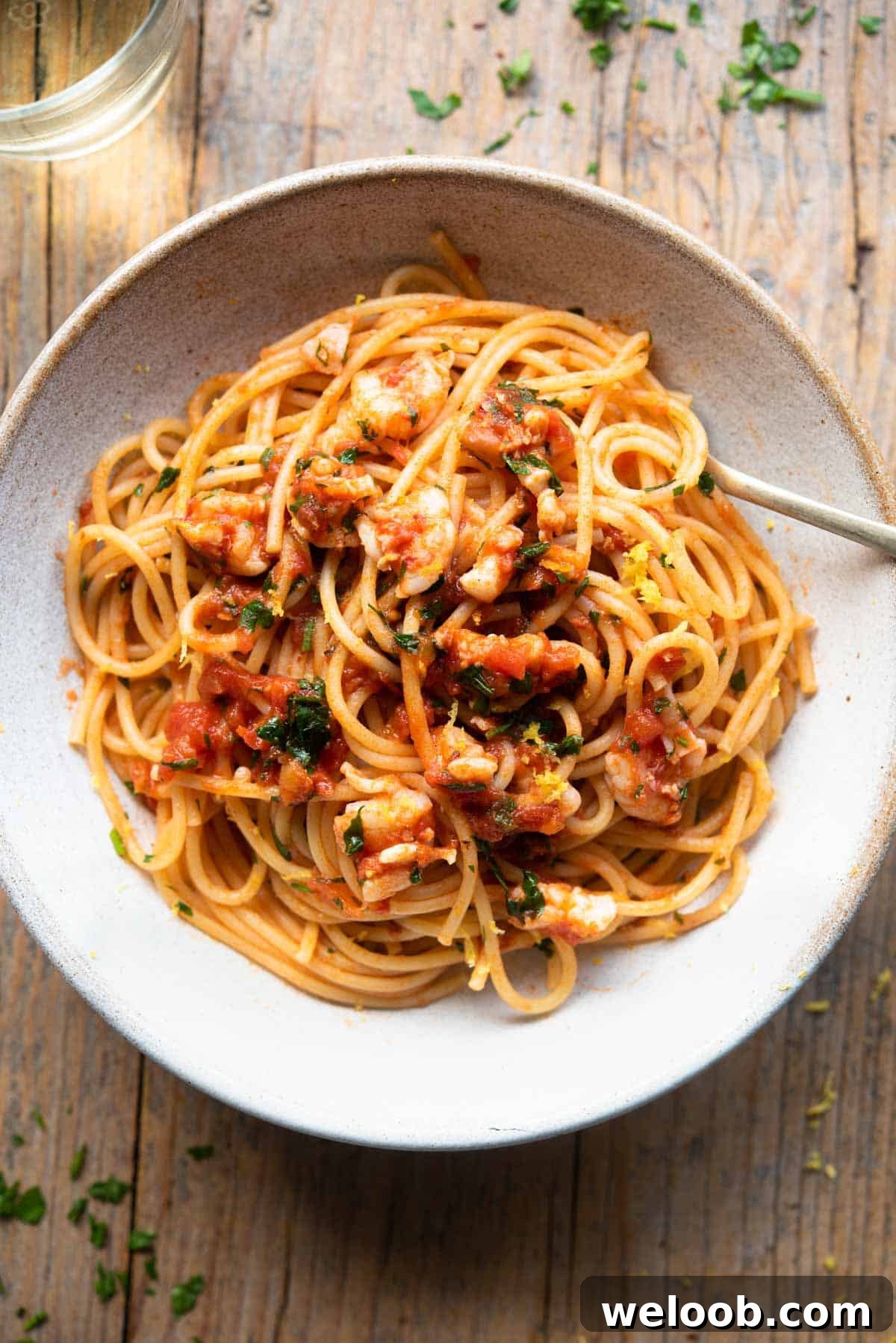 An overhead shot of shrimp spaghetti in a rustic bowl sitting on a wooden surface with a glass of white wine at the side.