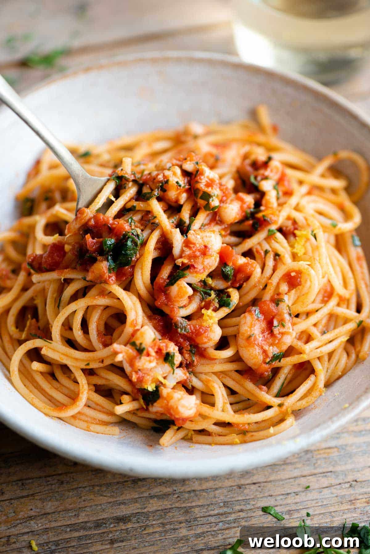 A close up side shot of shrimp spaghetti in a bowl with a fork at the side.