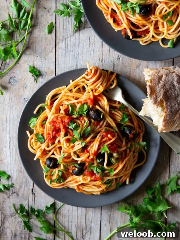 A plate of spaghetti with puttanesca sauce sitting on a wooden surface