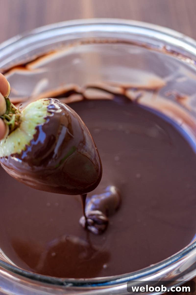hand holding a strawberry dipped in melted chocolate.