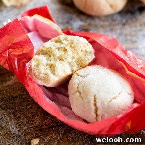 A close up of two amaretti cookies in a pink wrapper on a wooden surface.